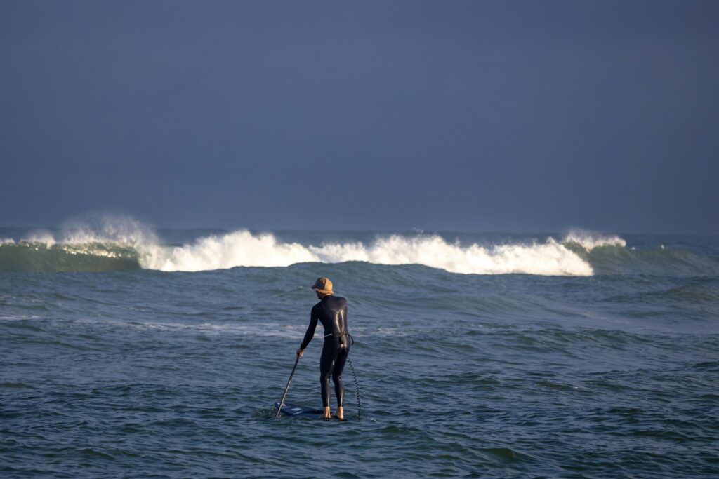 A lone paddleboarder in wetsuit enjoys the waves on a Danish sea, highlighting adventure and serenity.
